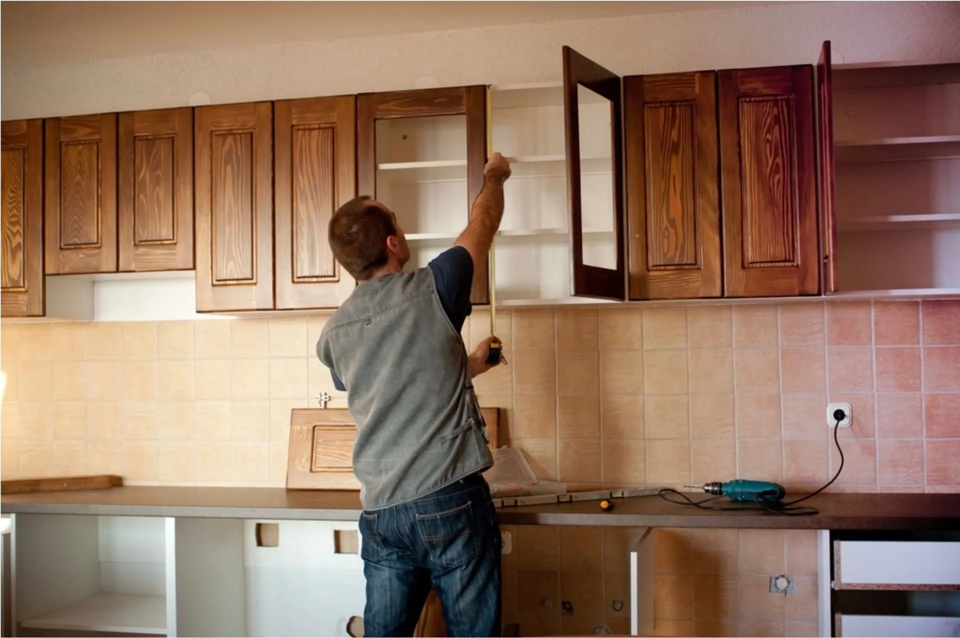 Carpenter measuring and installing stained wood cabinet doors during a kitchen update.