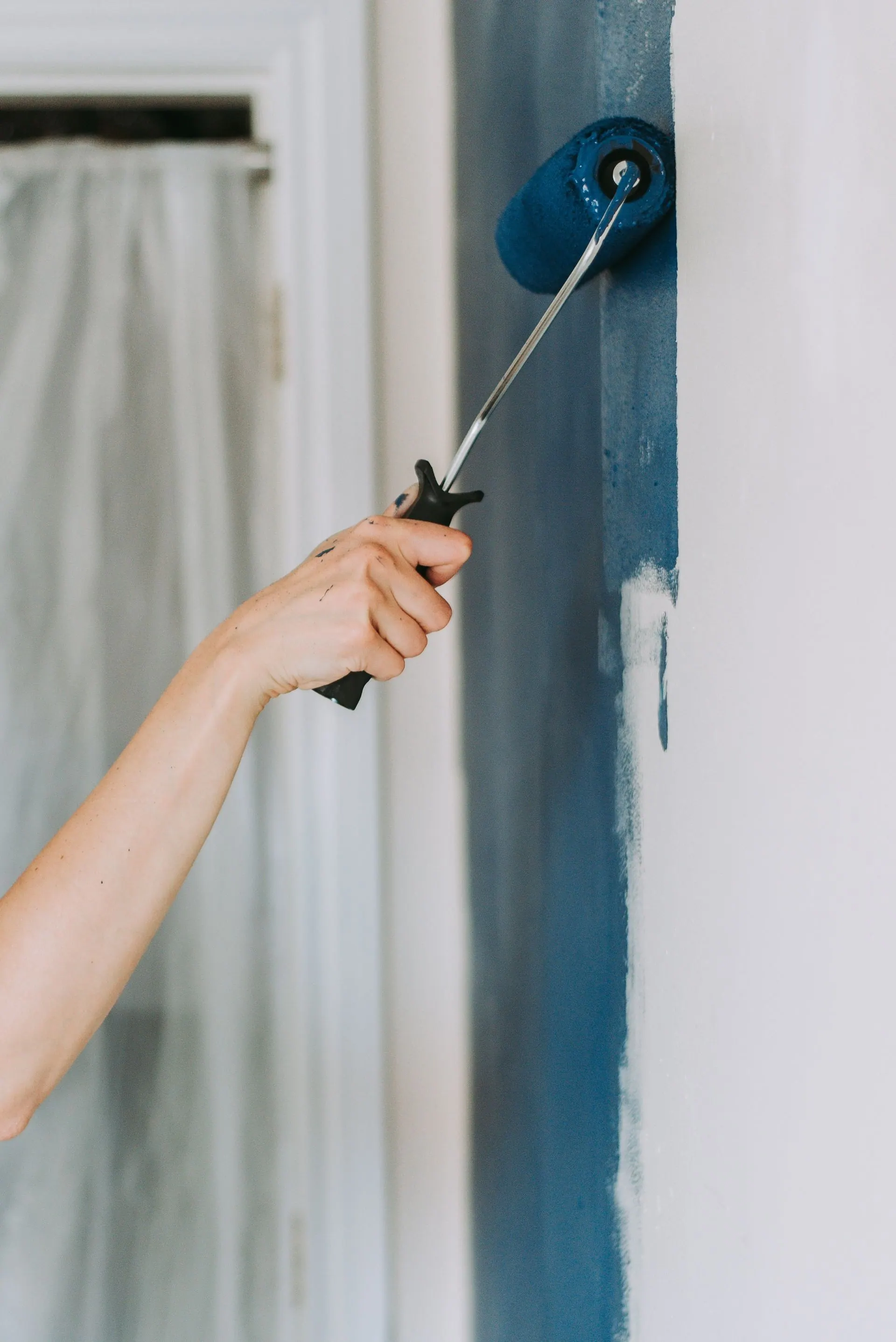 A close-up of a hand rolling deep blue paint onto an interior wall.