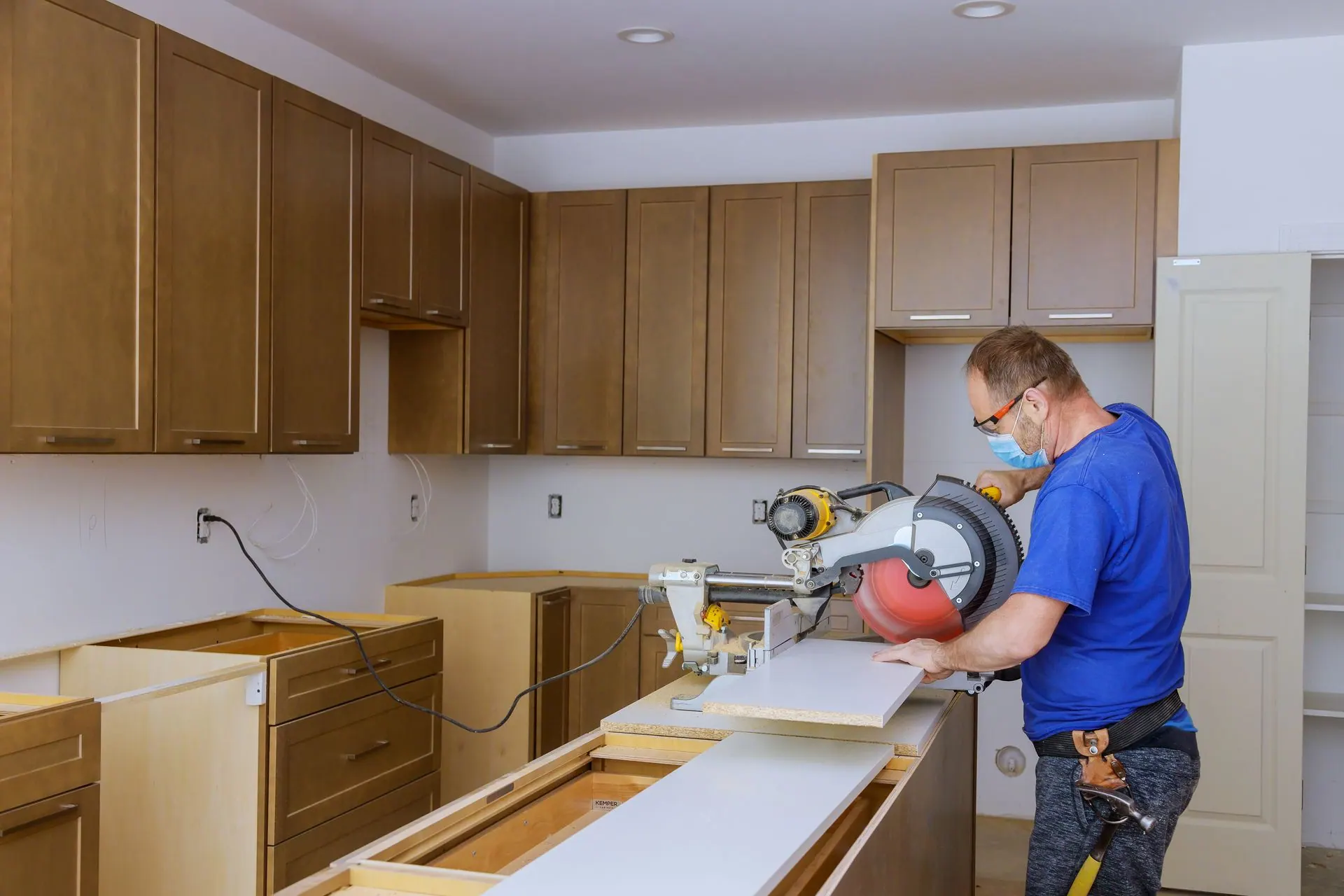 A contractor cuts a countertop with a miter saw during a kitchen cabinet remodel.