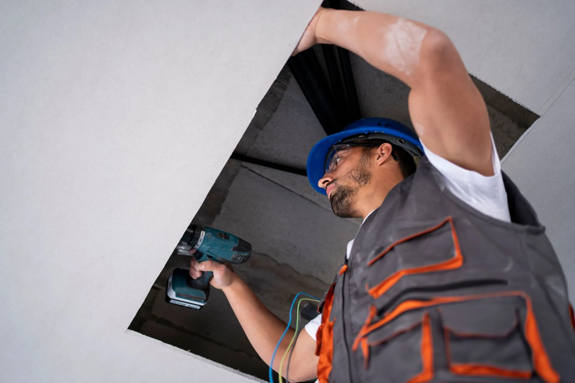 Worker driving screws into a ceiling panel while resetting loose fasteners on a Conover, NC drywall repair.