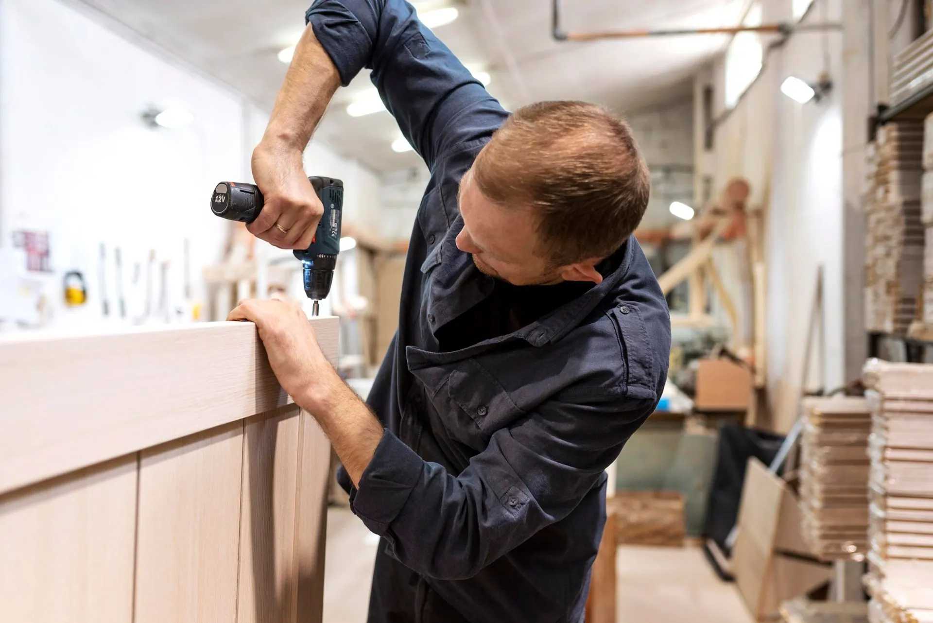 A woodworker drills into a cabinet door frame in a workshop.