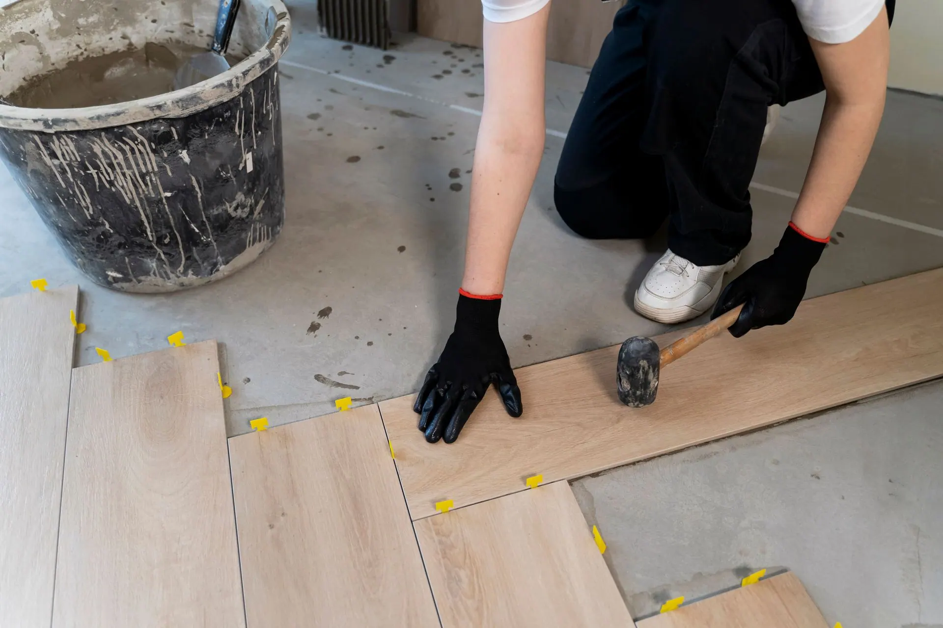Overhead view of a worker tapping wood-look vinyl plank flooring into place with a rubber mallet.