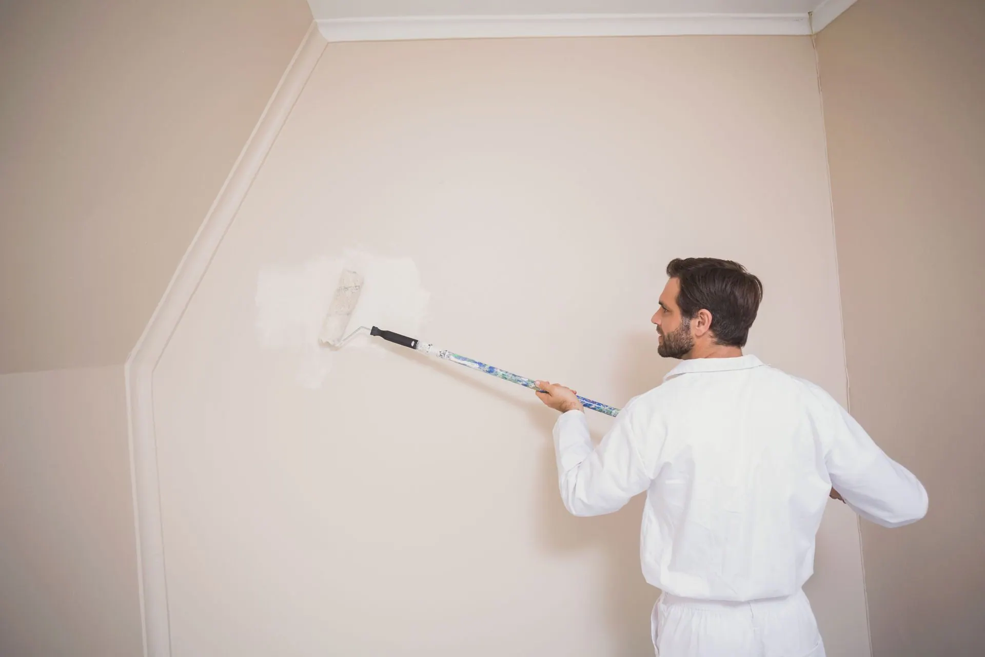 A painter in white coveralls rolls cream-colored paint onto an interior wall in Statesville, NC.
