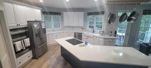 A renovated kitchen with white cabinets, a navy blue island, and hexagon tile backsplash.