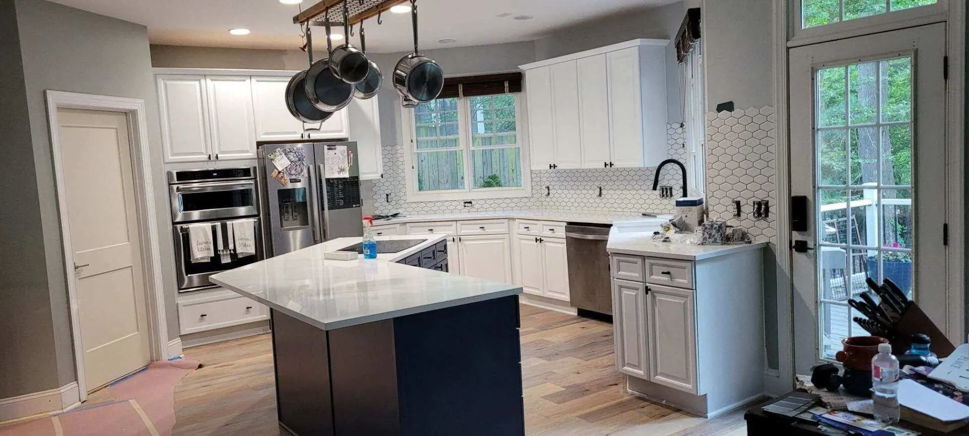 White cabinetry and a dark island in a finished kitchen near Denver, NC, with a hanging pot rack.