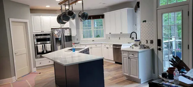 A kitchen renovation in progress with white cabinets, a navy island, and pots hanging from an overhead rack.